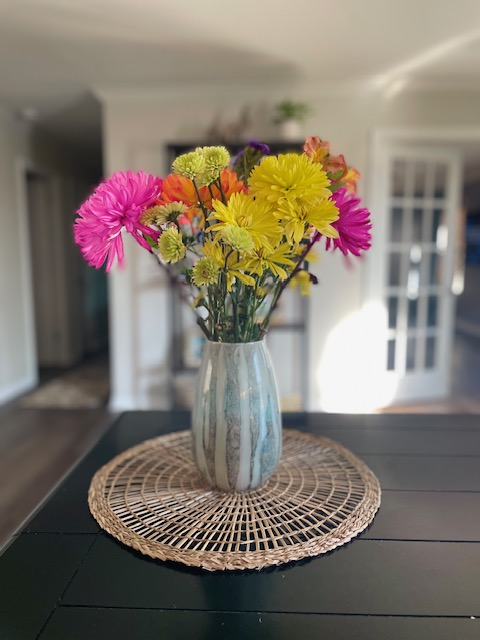 yellow, pink, and orange flowers in a green vase placed on a rattan placemat.